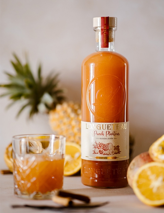 Bouteille de Punch Planteur et son verre servi entourés de fruits frais exotiques et épices